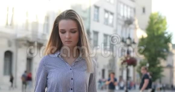 漂亮的金发女郎在一个闷热的日子里用她的手机和短信在街上散步视频的预览图