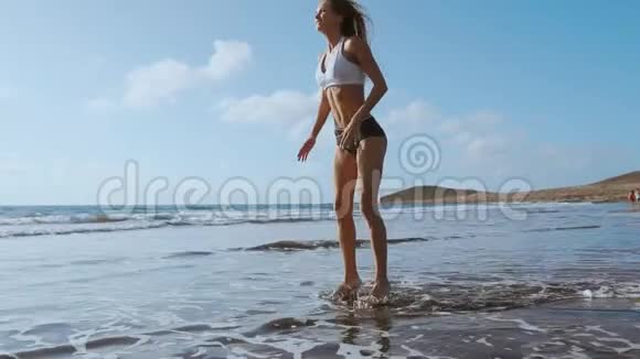 穿着运动服装短裤和t恤的女孩在加那利群岛海边的海滩上蹲着跳视频的预览图