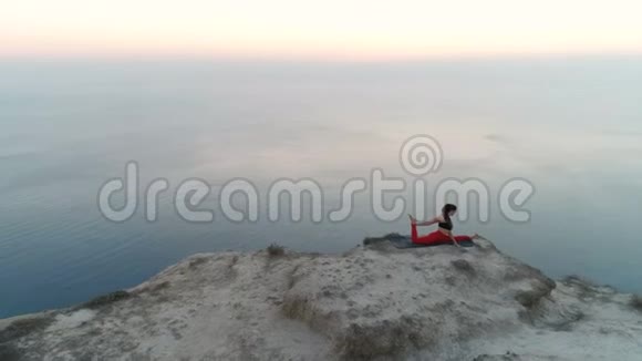 美丽的女人正在做瑜伽担架鸽子在山顶和海景日落空中镜头视频的预览图