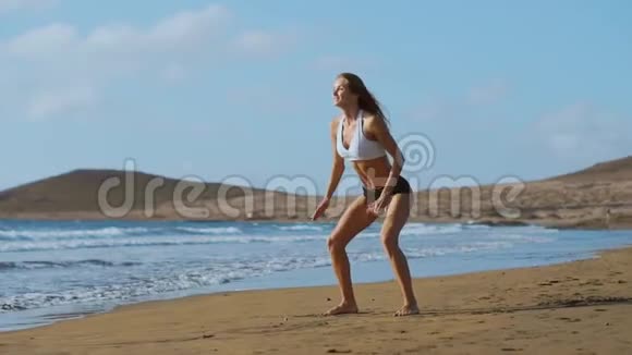 穿着运动服装短裤和t恤的女孩在加那利号附近的海滩上蹲着拍着跳视频的预览图