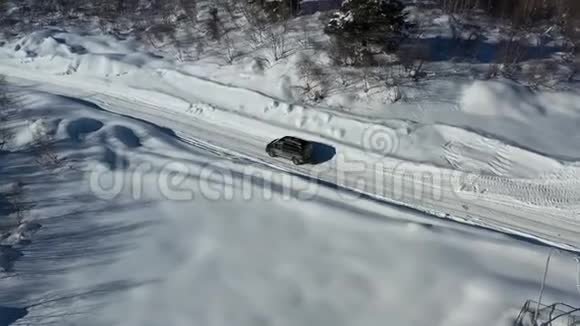 在一个阳光明媚的日子里黑色的面包车正在一条覆盖着雪的道路上行驶在4k的空中拍摄视频的预览图