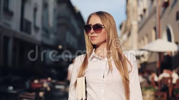 年轻迷人的女人带着太阳镜拿着书沿着老城散步学生教育发展激励视频的预览图