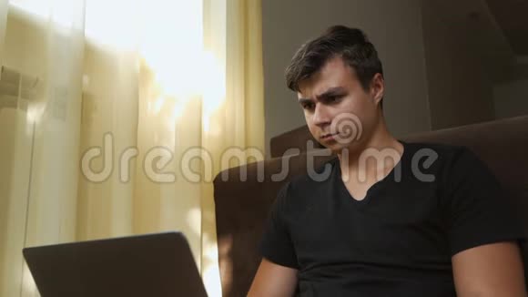 一个年轻人坐在窗边的房间里用笔记本电脑一个表情严肃的自由职业者视频的预览图