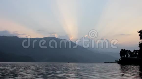 傍晚在湖上的双体船在夕阳的天空中在群山和阳光的映衬下视频的预览图