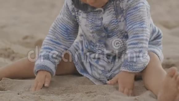 穿着针织连帽衫连衣裙的小女孩在日落海滩上玩沙子特写视频的预览图