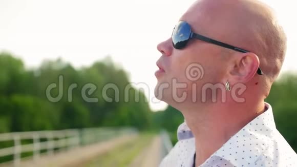 一位戴着太阳镜的秃头男子在一座废弃的铁路桥上唱歌近距离射击视频的预览图