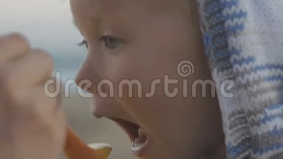 在海边背景上一个穿着针织连帽衫的金发婴儿用勺子喂着一只雌性手的特写镜头视频的预览图