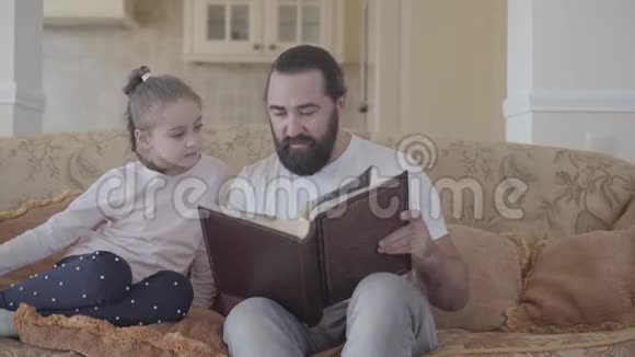 女儿和父亲坐在客厅里看着相册的画像里面有美好的回忆和有趣的故事视频的预览图