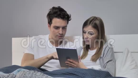 放松年轻夫妇在床上平板上浏览互联网视频的预览图