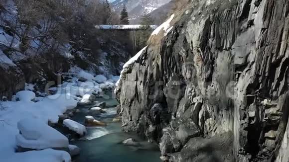 雪覆盖的岩石和高山河附近的高崖空中拍摄4k视频的预览图