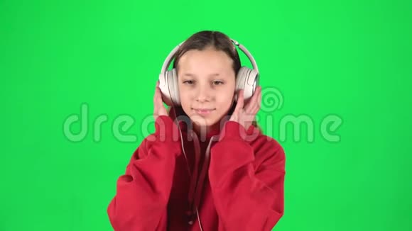 女孩听音乐在绿色背景上戴着白色的大耳机移动慢动作视频的预览图