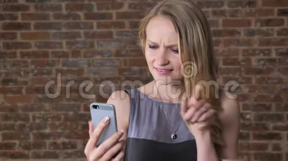 年轻可爱的金发女孩在智能手机上用视频聊天交流概念砖背景视频的预览图