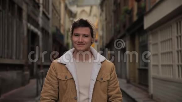 一位年轻时尚的帅哥在欧洲一个古老城镇的街道上对着镜头微笑的肖像视频的预览图