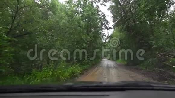 下雨时驾驶汽车行驶在森林的土路上交通恶劣的天气状况从小屋看视角视频的预览图