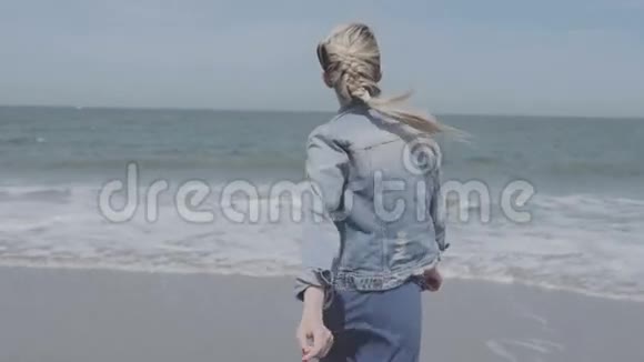 快乐的年轻女子穿着牛仔夹克在孤独的海滩上玩得开心视频的预览图