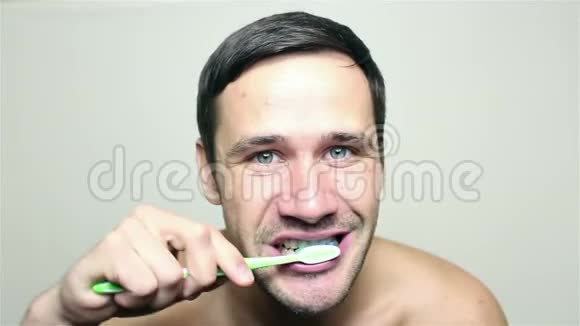 年轻的帅哥用绿色牙刷刷牙微笑着看着镜头视频的预览图