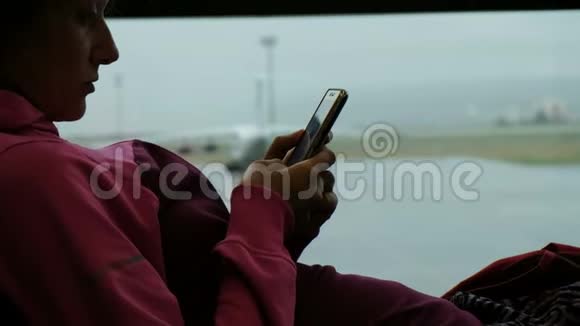 运动女性在机场窗口使用智能手机背景上的飞机视频的预览图