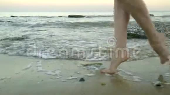 镜头从女性的双腿上升到一个穿着白色裙子的金发女郎在海滩上行走的脸视频的预览图
