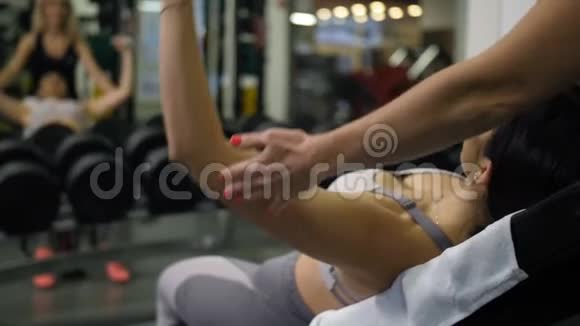 躺在长凳上用哑铃做运动的女孩一位女教练帮她做4K慢速运动视频的预览图