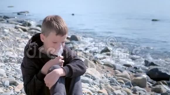 生病的孩子用雾化吸入面罩治疗哮喘坐在海边视频的预览图
