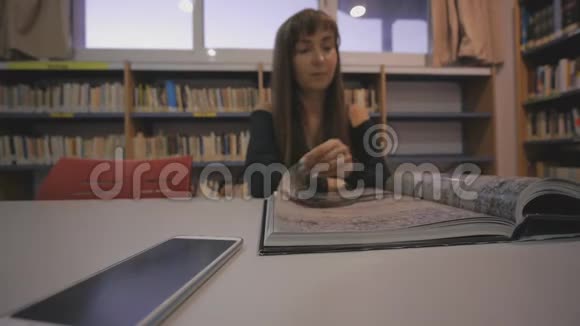 年轻的高加索女人在图书馆翻着插图书籍的一页视频的预览图
