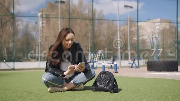 年轻女子使用手机坐在绿色草坪上视频的预览图