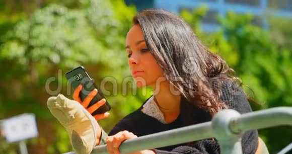 美丽的女人用手机而腿却伸在城市的栏杆上视频的预览图