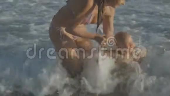 年轻的白人母亲抱着金发女婴跳进海浪中视频的预览图