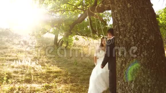 新娘和新郎在夏季公园的秋千上摇摆绳子在森林中的橡树枝上摆动视频的预览图