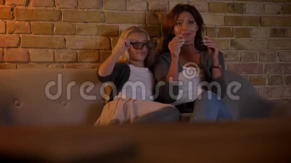 年轻的白种人女性和她的小女儿在家用3D眼镜看电视的特写镜头视频的预览图
