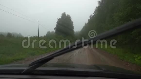下雨时驾驶汽车行驶在森林的土路上交通恶劣的天气状况从小屋看视角视频的预览图