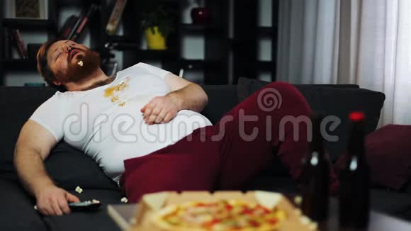 穿脏T恤的胖子睡在电视机前的沙发上视频的预览图