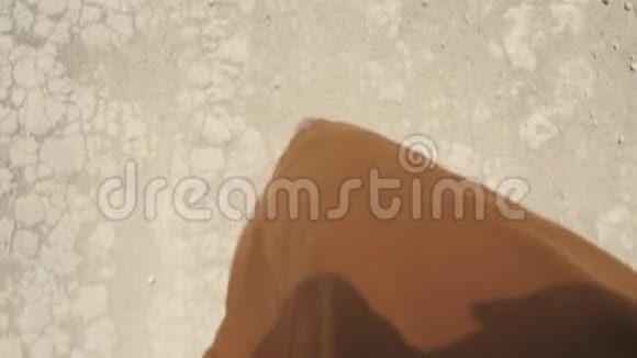 一个穿凉鞋和棕色连衣裙的女人走在干裂的地面上视频的预览图