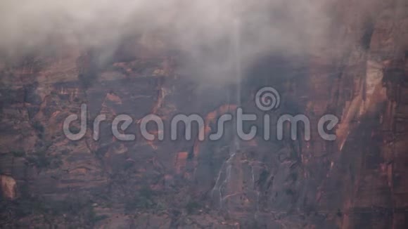 在锡安国家公园尤他州一个多雨的冬天云层低垂在悬崖上面对一个薄薄的瀑布倾泻在山坡上视频的预览图