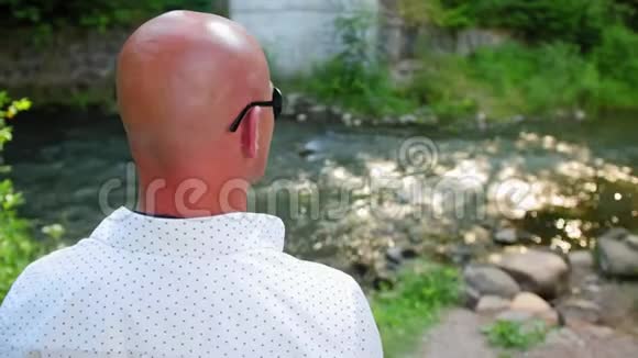 后景一个秃头男人看着一条河在桥下流淌近距离射击视频的预览图
