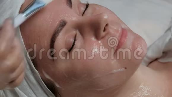 化妆师戴着透明手套用白色刷子在一个漂亮女孩的脸上涂上滋养霜女性美容p视频的预览图