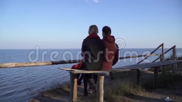 年轻夫妇坐在长凳上拥抱在水面的背景上在户外约会的情侣视频的预览图