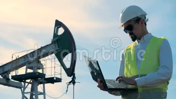 一名男性工人在一个运转正常的煤气井架旁边手提电脑的工作过程能源石油天然气燃油抽油机视频的预览图