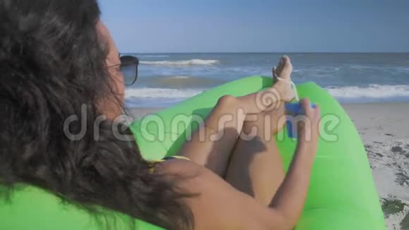 太阳眼镜中女人的特写镜头在海滩上喝鸡尾酒在海上看视频的预览图