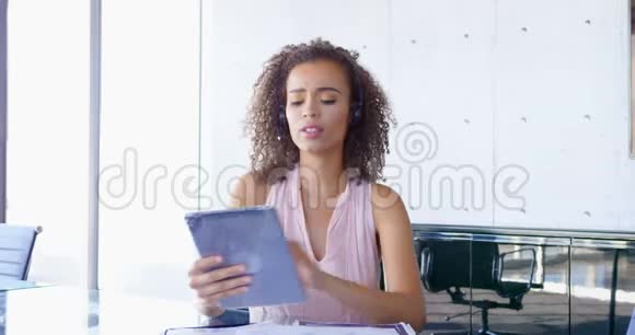 年轻的混血女商人在办公室的桌子上用耳机说话视频的预览图