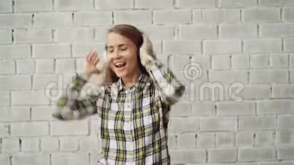 穿着时髦女性的无线耳机听收音机的欢快年轻女士跳舞唱歌的肖像视频的预览图