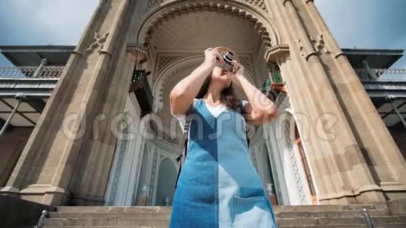 女专业摄影师戴墨镜帽用相机彩色雕刻大门拍照视频的预览图