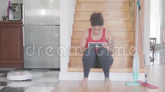可爱的非裔美国女人坐在大房子一楼的楼梯上在她的平板电脑上发短信现代视频的预览图