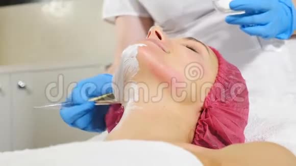在美容院戴面膜的漂亮女客户在女性脸上涂面膜用刷子视频的预览图