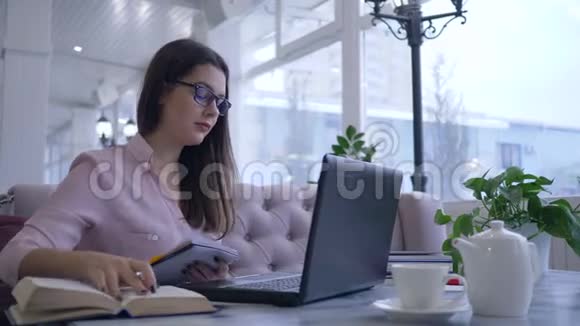 在线教育戴眼镜的女孩在现代上网本上的视频聊天中在笔记本上写笔记视频的预览图