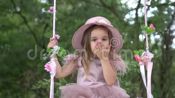 可爱的小女孩穿着漂亮的粉红色裙子骑在秋千上视频的预览图