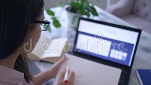 商务在线戴眼镜的漂亮女孩用笔记本电脑在笔记本电脑上写笔记用红色标记视频的预览图