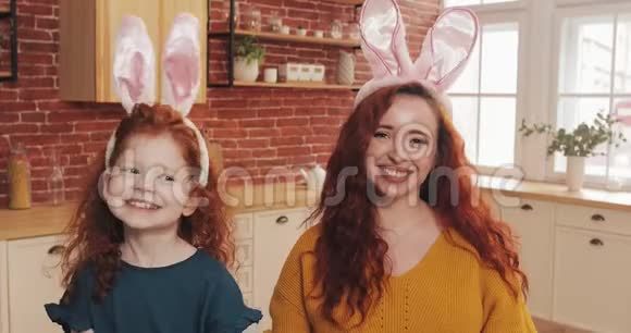 复活节快乐性格开朗的红发小女孩和妈妈一起穿着兔耳制作视频聊天或与亲戚聊天视频的预览图