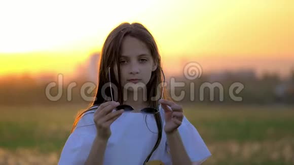 闭上漂亮的小女孩戴上太阳镜在日落时在户外弹吉他更有趣的表情模仿流行视频的预览图