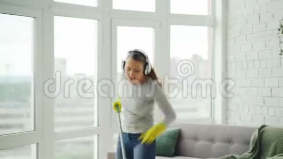 快乐的年轻金发女郎正在做家务在现代的房子里玩得很开心她正在用拖把唱歌和跳舞洗地板视频的预览图